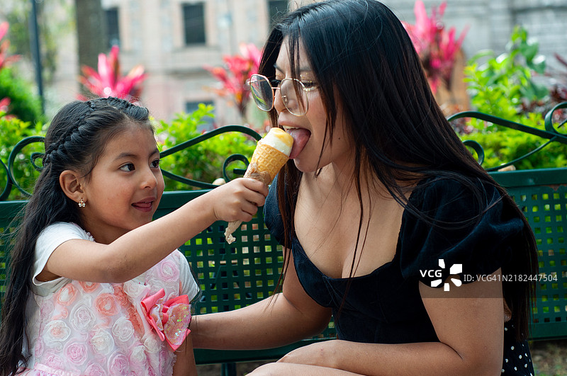 温馨的场景，小女孩满怀爱意地与妈妈分享冰淇淋，周围洋溢着笑容。图片素材
