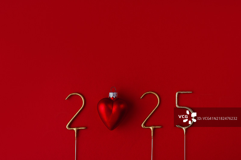 红色表面上的金色2025数字与心形新年玩具相结合。图片素材