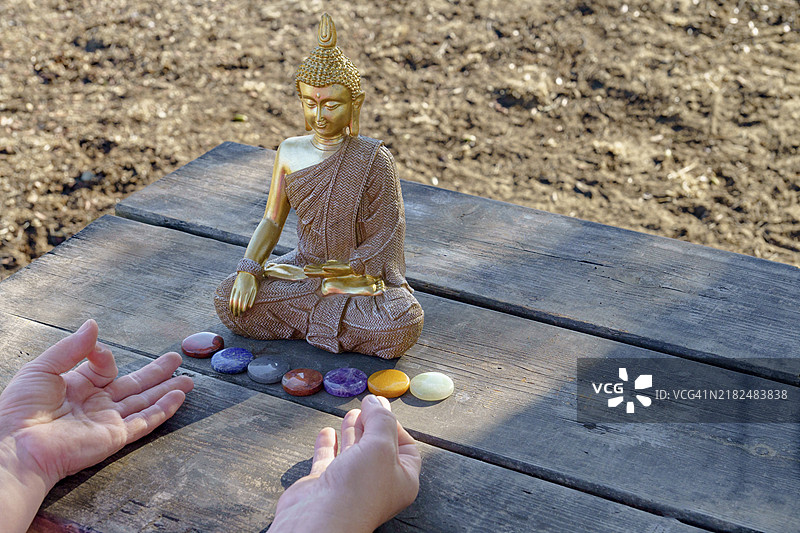 女人的手在阳光明媚的公园里，佛像前冥想，木桌上摆放着五彩的脉轮石。图片素材