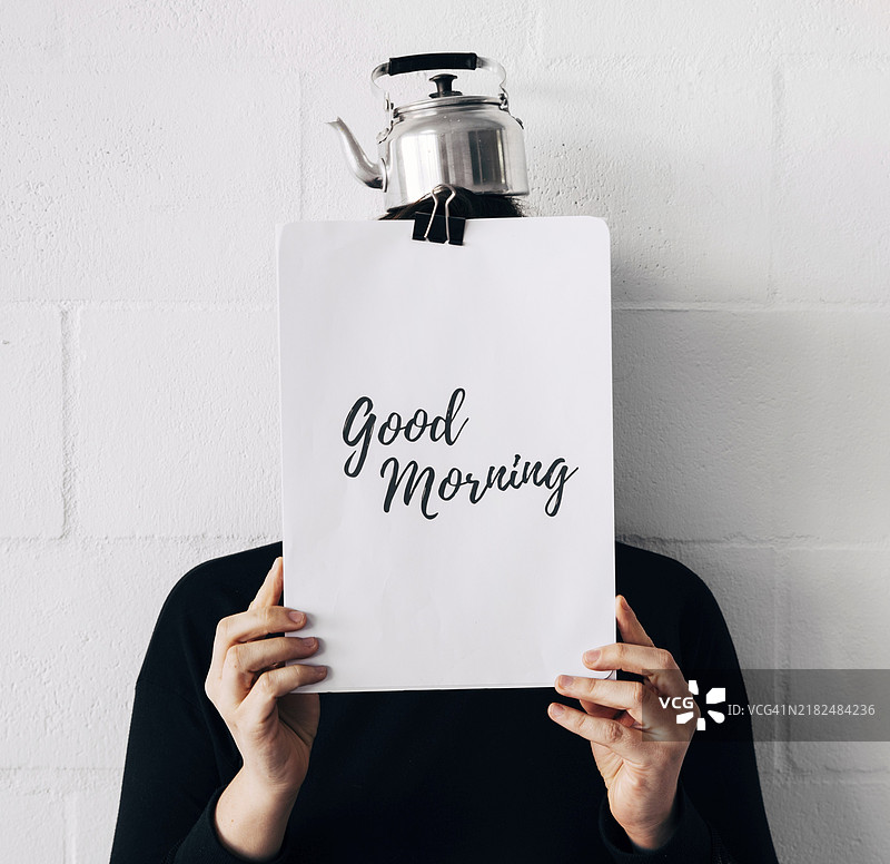 女人用水壶做头，手持早安信息纸，面朝白墙。图片素材
