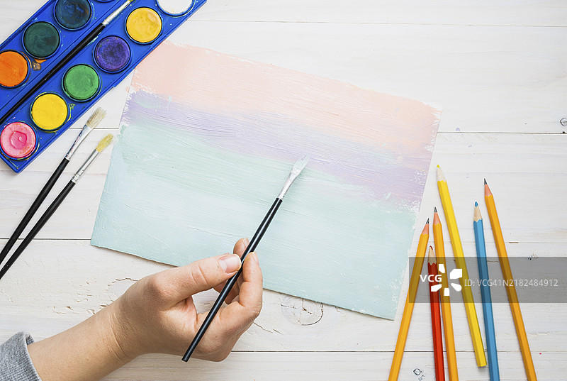 一个人用水彩画笔在桌子上绘画纸张图片素材