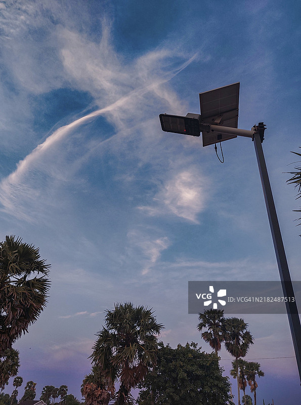 夕阳下，带有云朵和棕榈树的天空中，太阳能街灯的剪影，体现可持续生活。图片素材