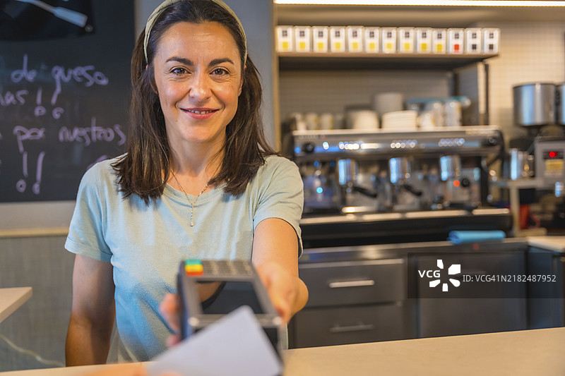 一位棕发的白人女服务员微笑着将数据终端递给顾客，以便用信用卡进行支付。图片素材