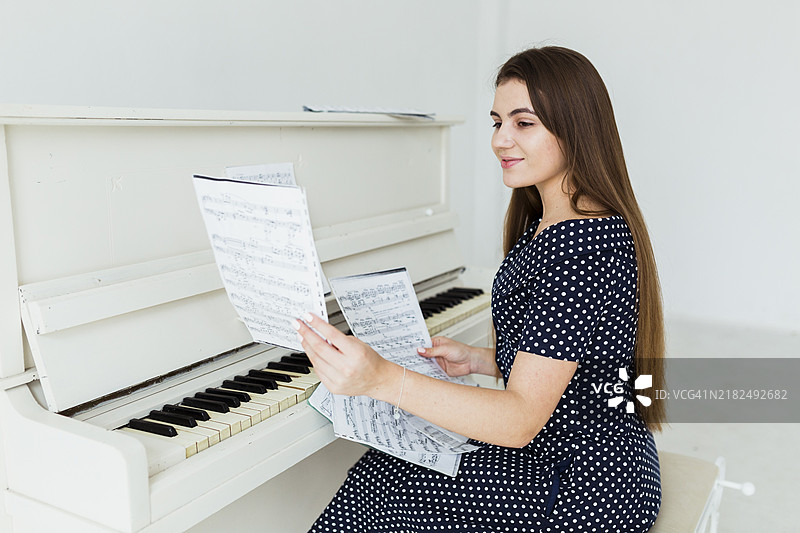 微笑的年轻女性坐在钢琴前看乐谱图片素材