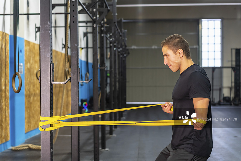 一位运动型男子在交叉训练健身房使用弹力带训练，左臂截肢。图片素材