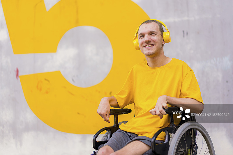 一位穿着黄色衣服的残疾人坐在轮椅上，微笑着听音乐。图片素材