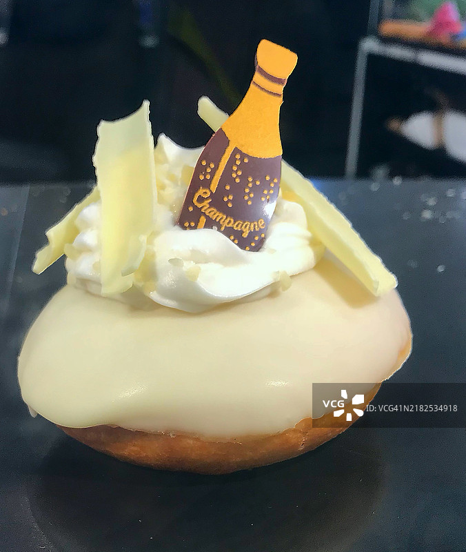 毕业杯子蛋糕，上面装饰有白巧克力糖霜、新鲜奶油和香槟瓶糖饰。香草海绵蛋糕，拍摄于2024年9月的英国面包店。图片素材