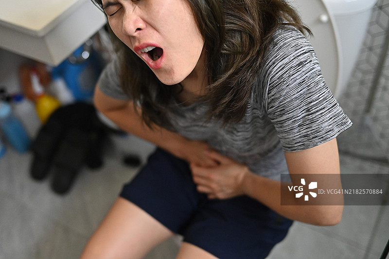 亚洲女性坐在厕所上，腹部疼痛的特写镜头。腹痛是腹部的痉挛或钝痛。图片素材