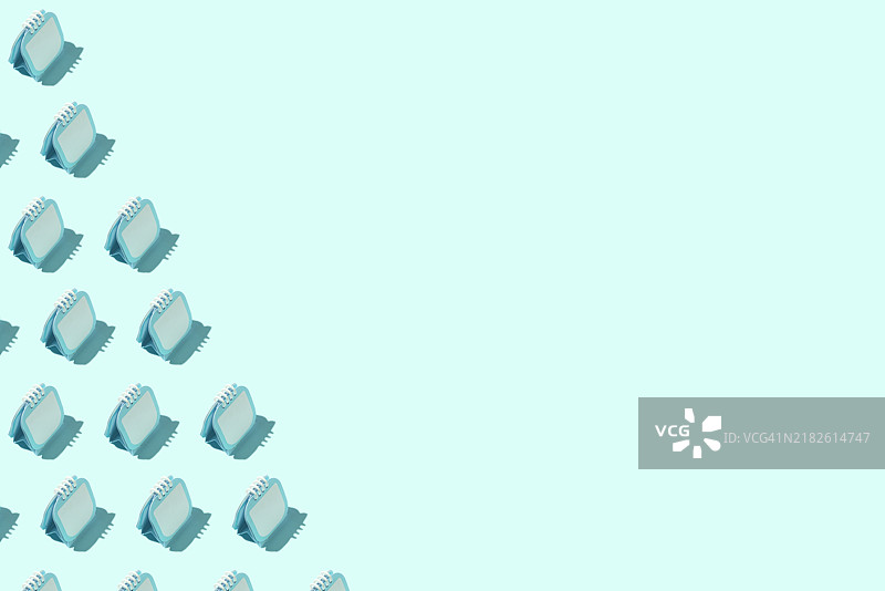 青色背景上有青色活页夹日历记事本的图案。概念包括截止日期、日期、笔记、周、年、年鉴、设计、图案和创意。图片素材