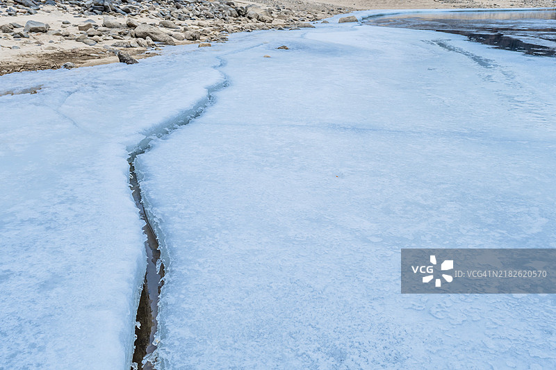 一条冰冻的河流，显著的裂缝穿过覆盖着雪的冰面，位于韩国图片素材