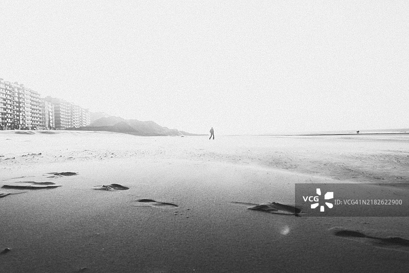 孤独的人影在空旷的黑白沙滩上，背景是大海。比利时，米德尔基尔克，欧洲图片素材