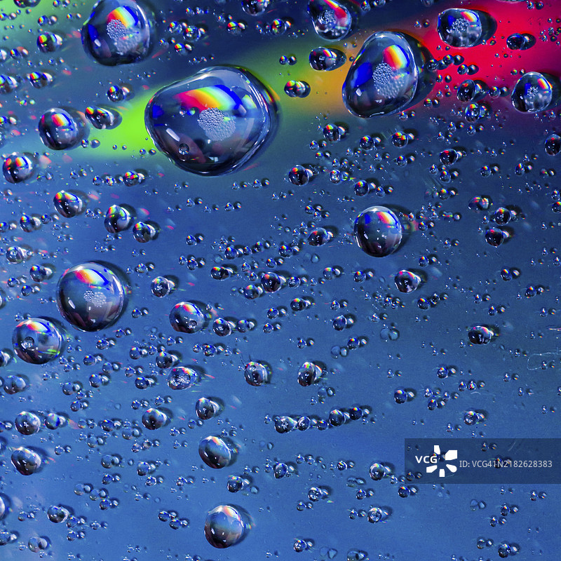 蓝色背景上的水滴特写，顶部有彩虹色条纹穿过图像。图片素材