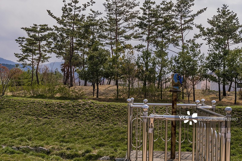 公园里用于开启小型闸门的旧手摇曲柄，背景是一片常青树树林。图片素材