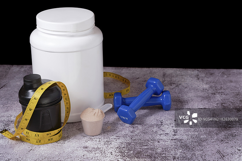 黑色背景上的乳清蛋白粉、摇摇杯、卷尺和哑铃，留有空白空间图片素材
