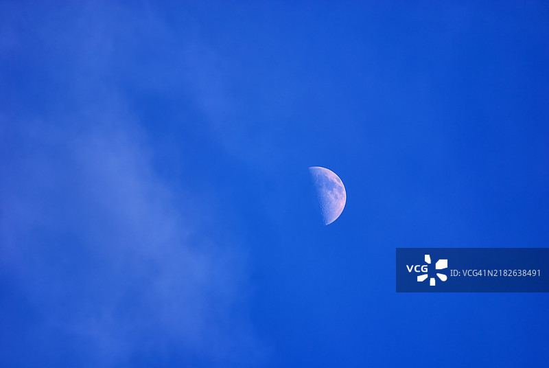 半月挂在多云的蓝天中。图片素材