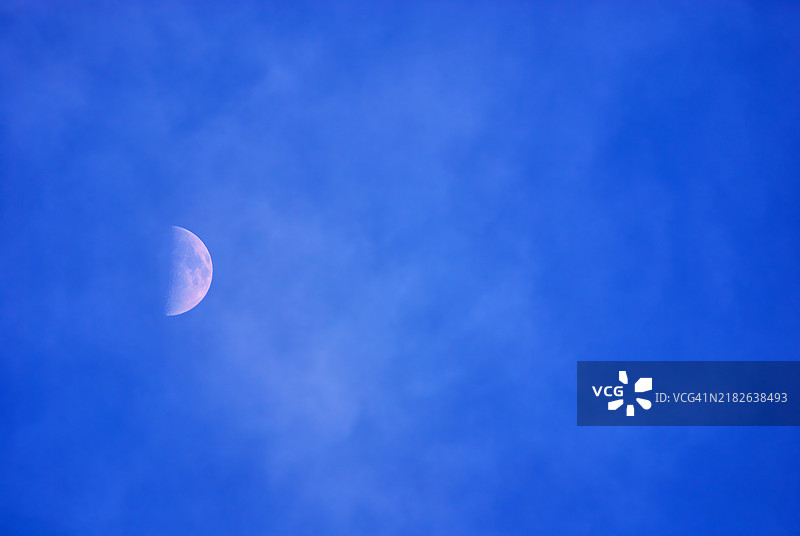半月挂在多云的蓝天中。图片素材