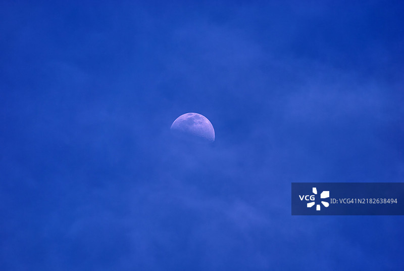 半月挂在多云的蓝天上。图片素材