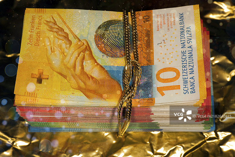 瑞士黑色资金的象征照片，瑞士钞票放在金色封面上，周围缠绕着金链，工作室摄影，黑色背景。图片素材