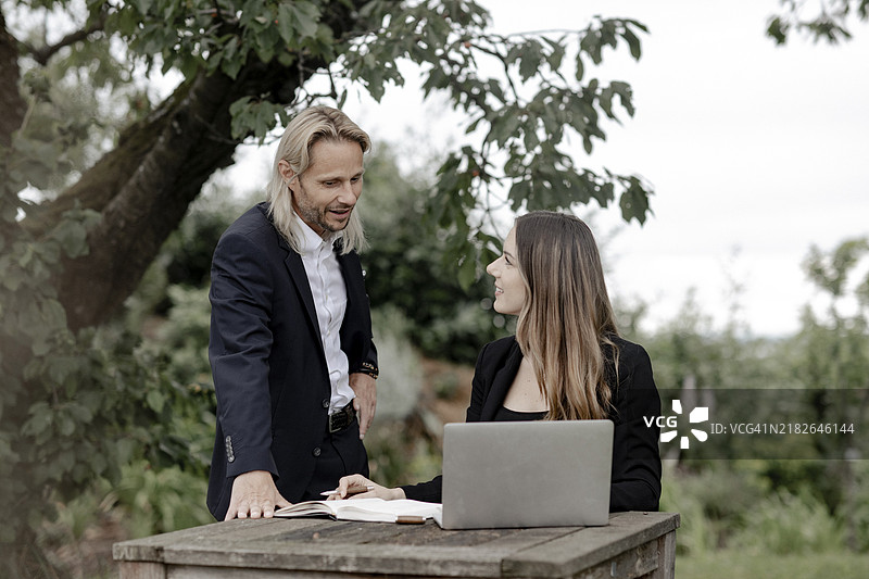 在木桌上，商人和女商人正在户外使用笔记本电脑工作图片素材