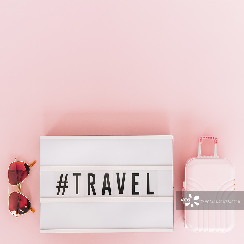 带有旅行文字的灯箱，配有太阳镜和迷你旅行包，粉色背景图片素材