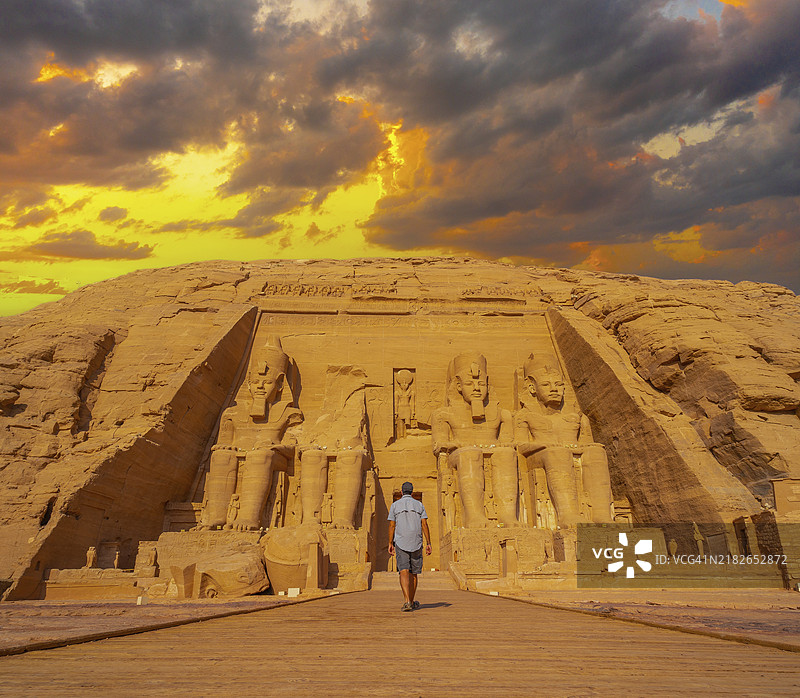 一名年轻男子走向位于埃及南部努比亚的阿布辛贝尔神庙，旁边是纳赛尔湖。拉美西斯二世的神庙，旅行生活方式。图片素材