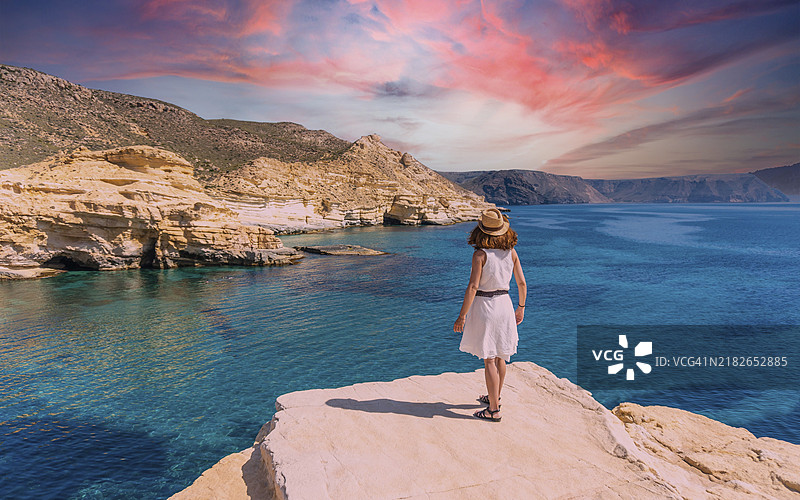 一位穿着白色裙子的年轻女性在阿尔梅里亚的卡博德加塔罗达尔基拉尔的美丽夏日里凝视着海洋，地中海，西班牙。图片素材