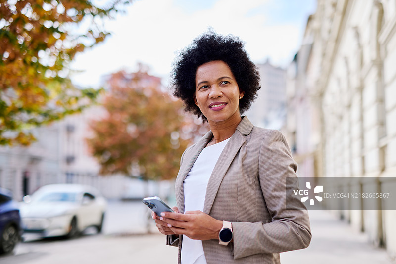 自信的女商人在城市环境中户外拿着智能手机图片素材