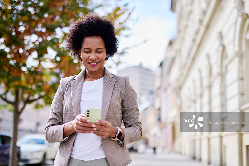 自信的女商人在城市环境中户外拿着智能手机图片素材