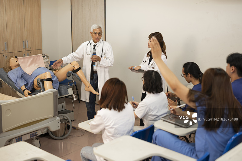 一位年轻的亚洲女性产科医生和一位经验丰富的资深教授在产科学教室里，使用人体模型向年轻学生教授女性医学专业知识，并培训他们的护理专业技能。图片素材