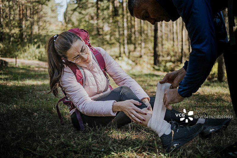 徒步旅行者在阳光明媚的森林中因脚踝受伤接受急救。图片素材
