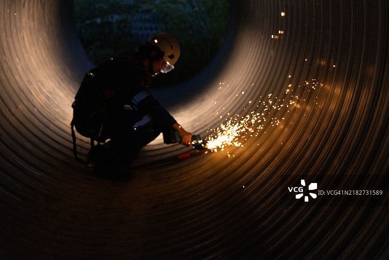 在管道中打磨重金属。工人使用电动磨光机。图片素材