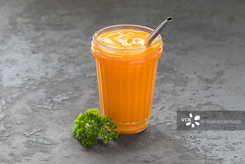 胡萝卜饮料，玻璃杯中的冰沙，配有吸管。深灰色背景。图片素材