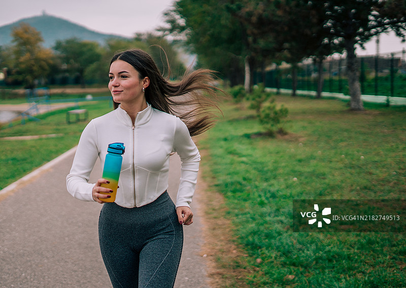 一位年轻女性在晨光中跑步，穿着反映她活力和奉献精神的运动装备。图片素材