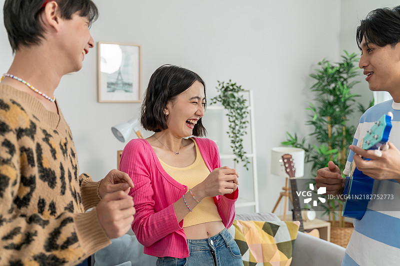 年轻的亚洲朋友们在家中的客厅里享受音乐舞蹈。迷人的男女在唱歌和弹尤克里里，分享欢笑时刻，共同庆祝他们的友谊。图片素材