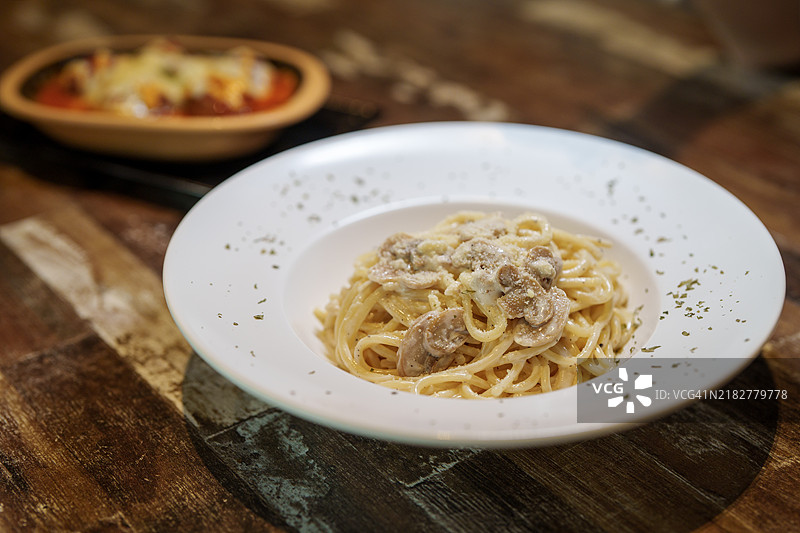 一盘新鲜上桌的奶油蘑菇意大利面特写，摆放在餐厅的木桌上。图片素材