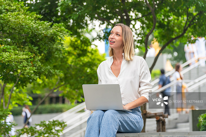 户外使用笔记本电脑的女性，满意地望向远方图片素材