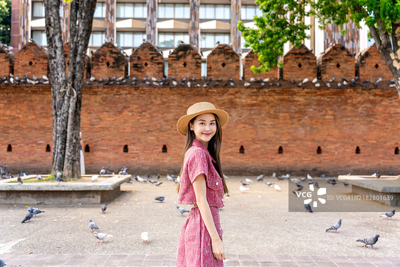 快乐的亚洲女性在清迈塔佩门的历史砖墙前被鸽子围绕图片素材