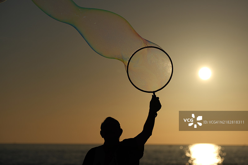 在日落时分，一个男人展示着一个发光的肥皂泡。图片素材