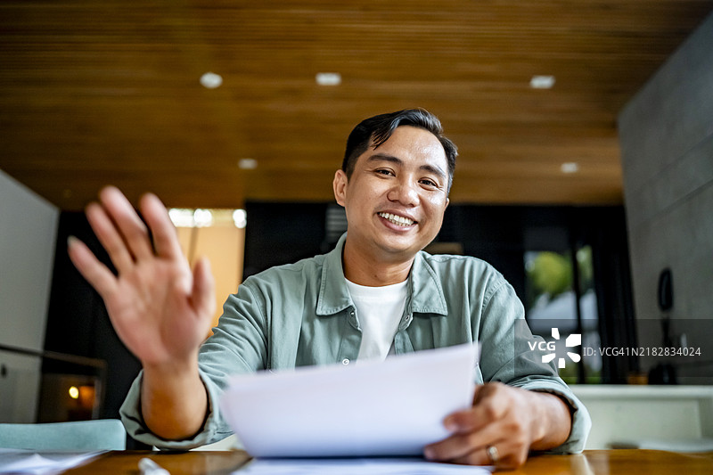 在家中参加虚拟会议时挥手的快乐男士图片素材