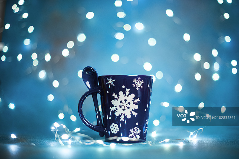 节日蓝色雪花图案杯与闪烁的节日灯光图片素材