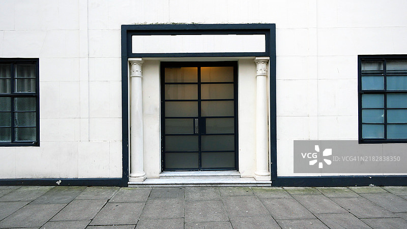 伦敦，英格兰，英国一栋住宅建筑的前门特写。白色和黑色的外立面，带有盲窗。复古风格的建筑。铺砌的人行道。阳光。自然色彩和风化效果。图片素材