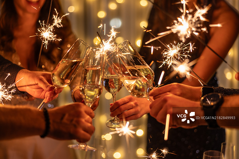 年轻朋友在夜总会举杯碰杯庆祝香槟。快乐的人们在派对上手持烟花。庆祝、人与节日的概念。图片素材
