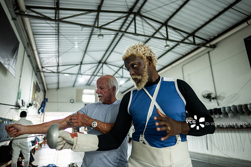 教练在健身俱乐部帮助男子练习击剑图片素材