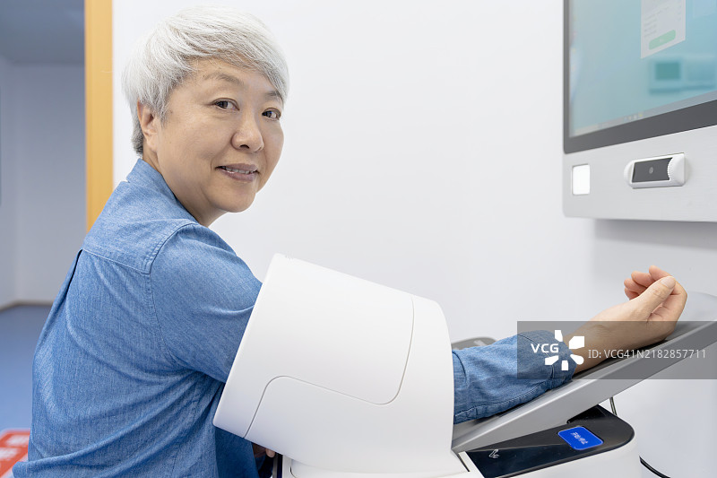 亚洲老年女性正在用数字血压计自测血压和心率图片素材