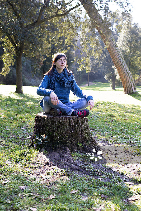 一位西班牙裔女性坐在砍伐的树干上，放松地看着镜头，身处大自然中。图片素材