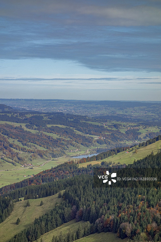 秋季色彩的广阔山脉景观，森林在蓝天之下，位于德国巴伐利亚的奥伯斯陶芬，阿尔高地区。图片素材
