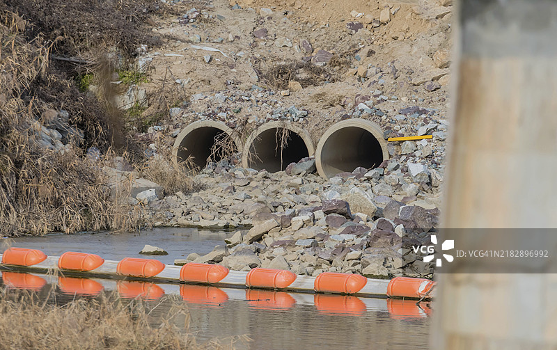 山坡旁的三个排水涵洞，流入浅河。前景中的桥支柱模糊不清。图片素材