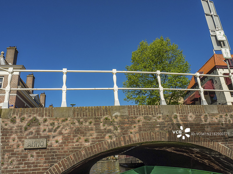 阿尔克马尔，荷兰，蓝天之下，树木和古老建筑旁的白色栏杆砖桥图片素材