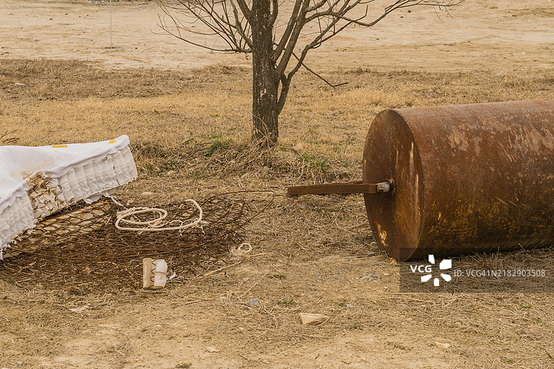 冬天的公园里，废弃的床垫旁边有一棵小树和一个手动表面滚筒。图片素材