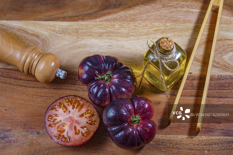 从上方俯视一组美味的新鲜蓝色番茄，旁边有一些木制夹子、橄榄油和一个胡椒瓶，放在木桌上。图片素材